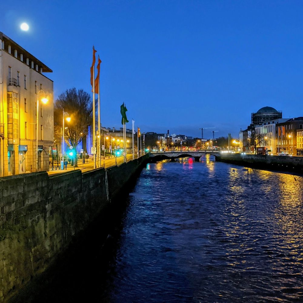 Die Liffey-Kais in Dublin zur blauen Stunde, beleuchtete Straßenlaternen und eine Brücke im Hintergrund