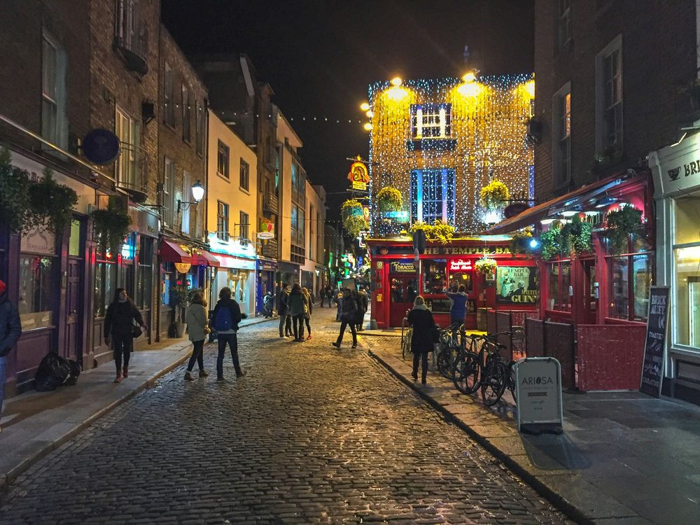 Kopfsteinpflastergasse in Temple Bar bei Nacht mit Lichterketten über der Straße und Passanten