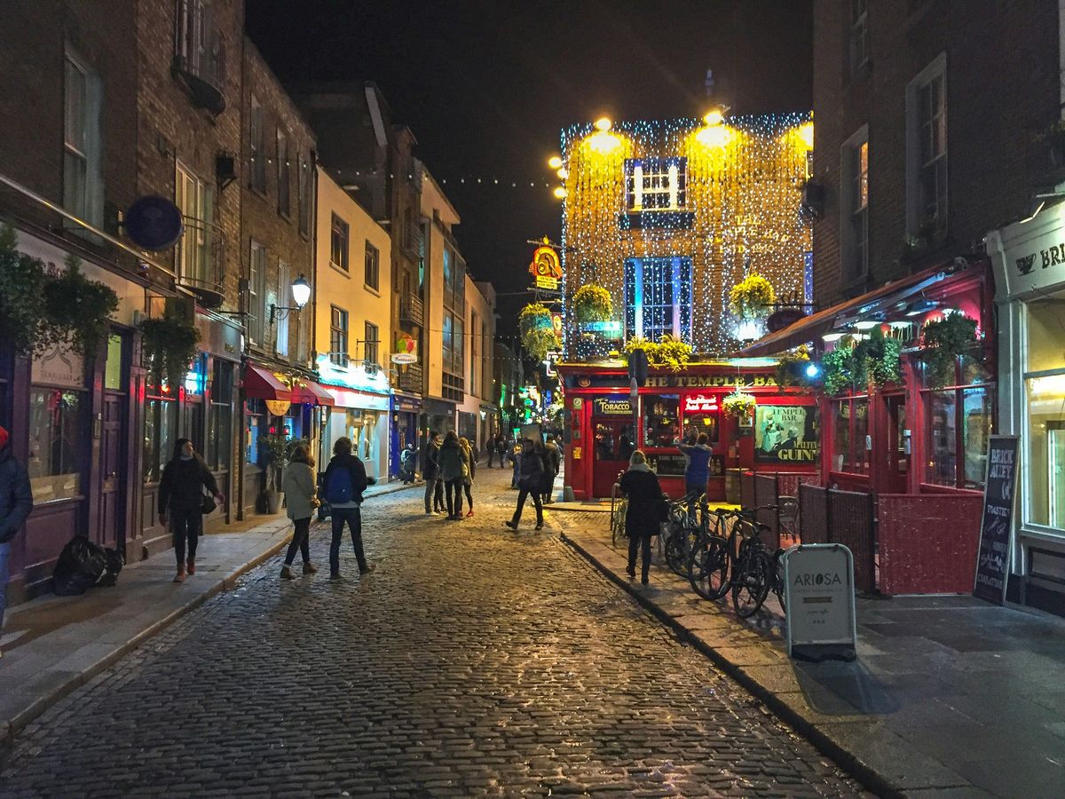 Kopfsteinpflastergasse in Temple Bar bei Nacht mit Lichterketten über der Straße und Passanten