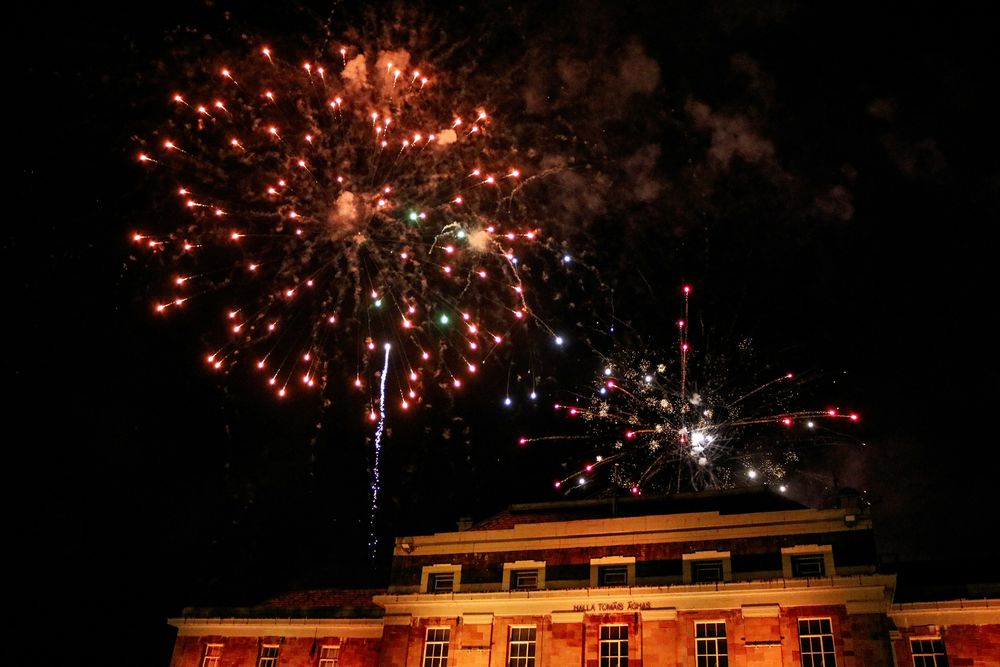 Feuerwerk explodiert in Rot und Weiß am Nachthimmel über einem angestrahlten Sandsteingebäude
