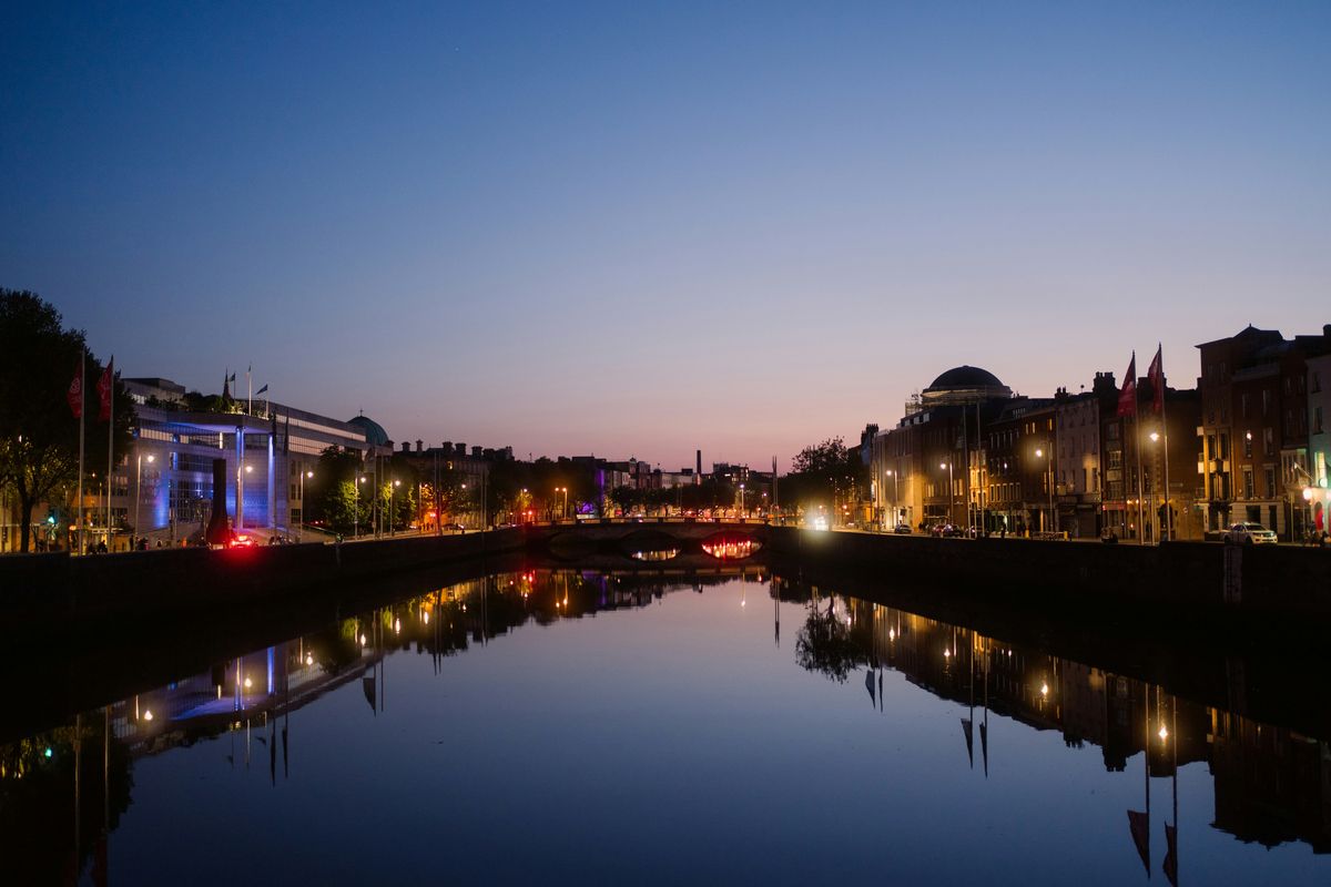 Die Liffey in Dublin bei Abenddämmerung, spiegelglattes Wasser, beleuchtete Kais und die Kuppel der Four Courts
